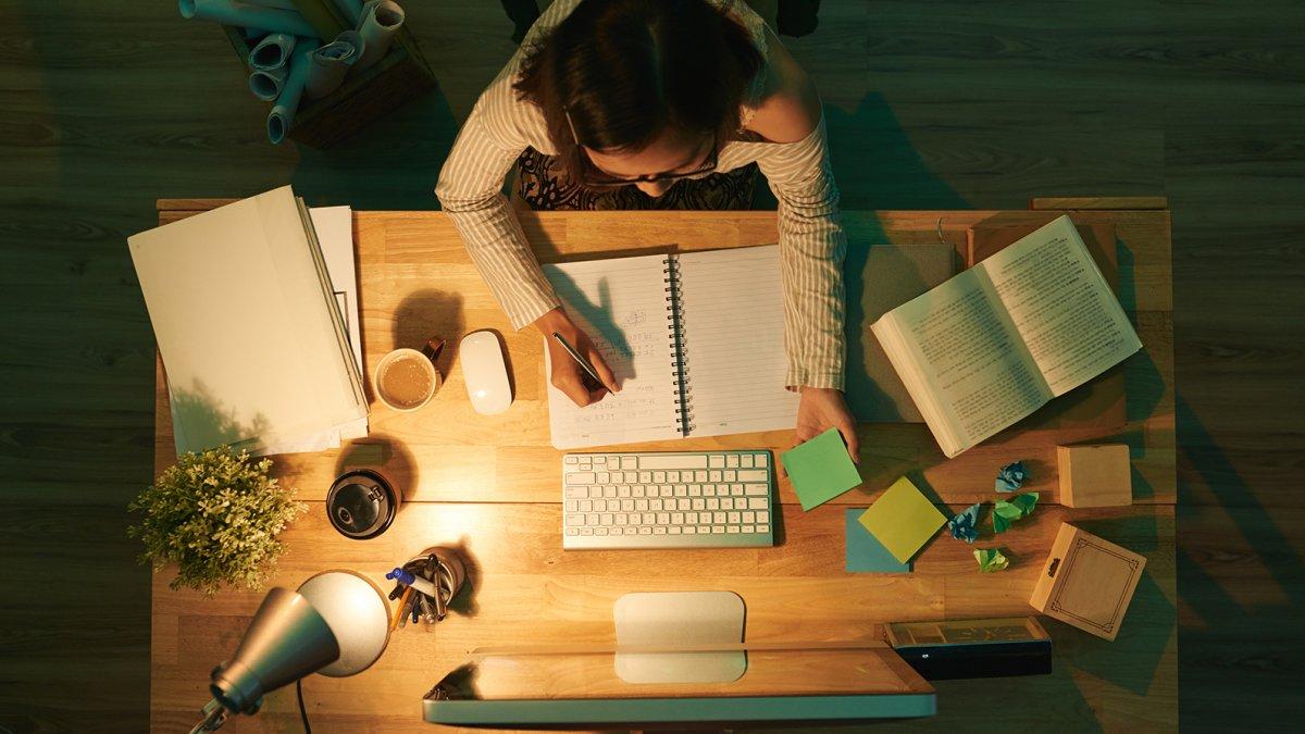 An English major at her desk, seen from directly above. On the desk are various books, notebooks, a computer, and the necessary cup of coffee.