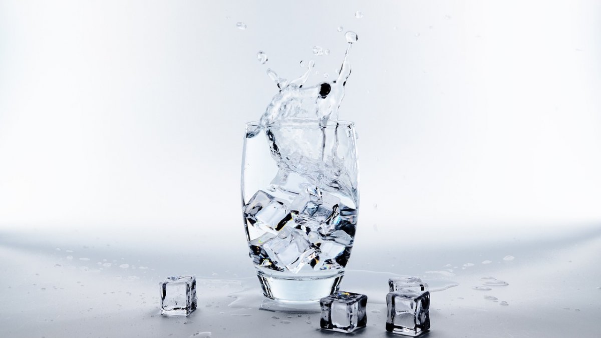 Glass cup with ice splashing in water
