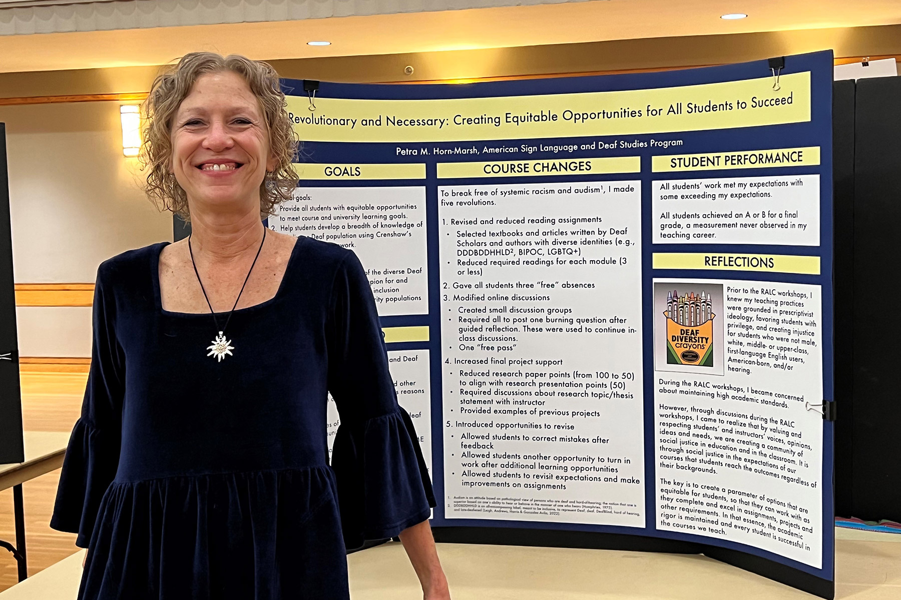 A smiling professor, Petra Horn-Marsh, stands next to a display of course changes inspired by the Revolutionizing Academia workshops, taught by Chanelle Wilson. 