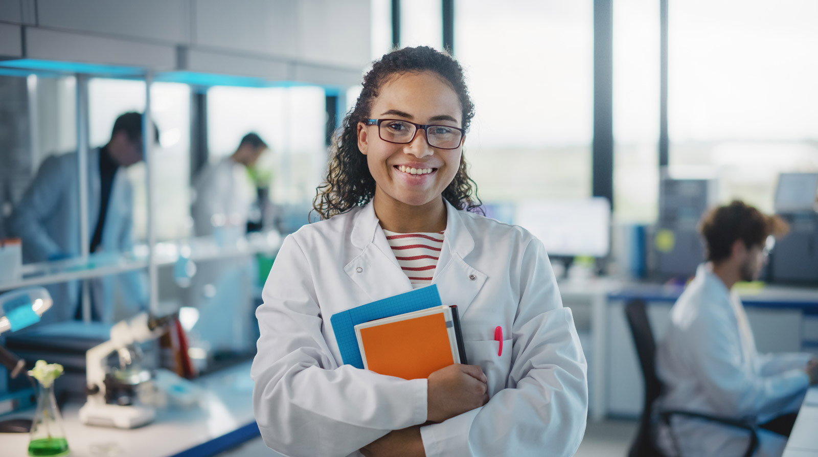 A woman in a lab coat holding books smiling. 