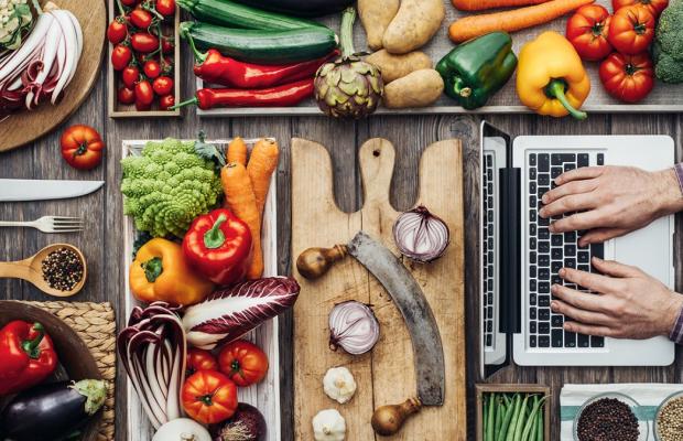 Overhead view of table with lots of vegetables and person working on laptop