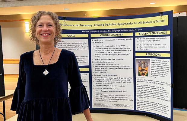 A smiling professor, Petra Horn-Marsh, stands next to a display of course changes inspired by the Revolutionizing Academia workshops, taught by Chanelle Wilson. 
