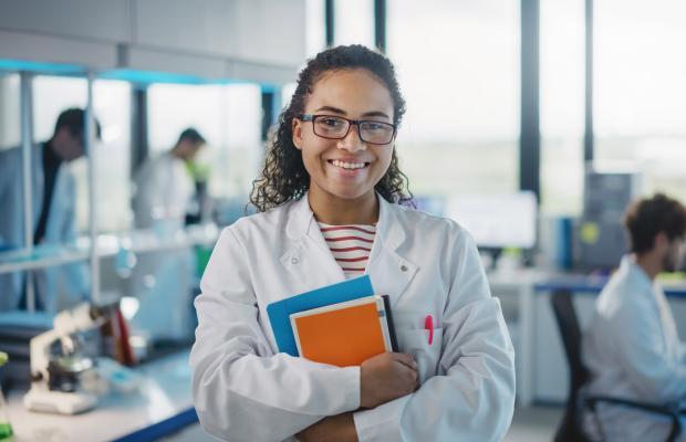 A woman in a lab coat holding books smiling. 