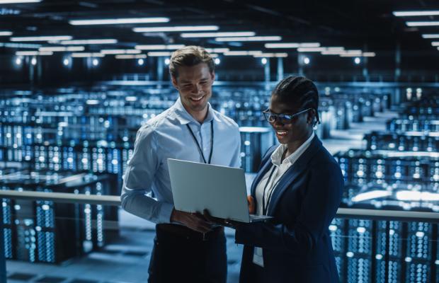 Two people standing in front of computer servers talking 